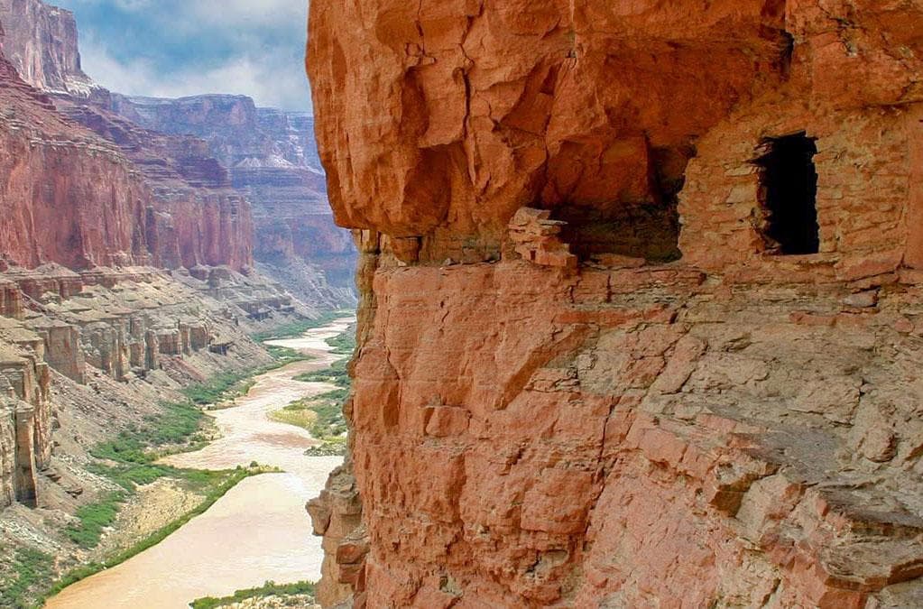 a small ancestral masonry storage room in a cliff above a muddy river.